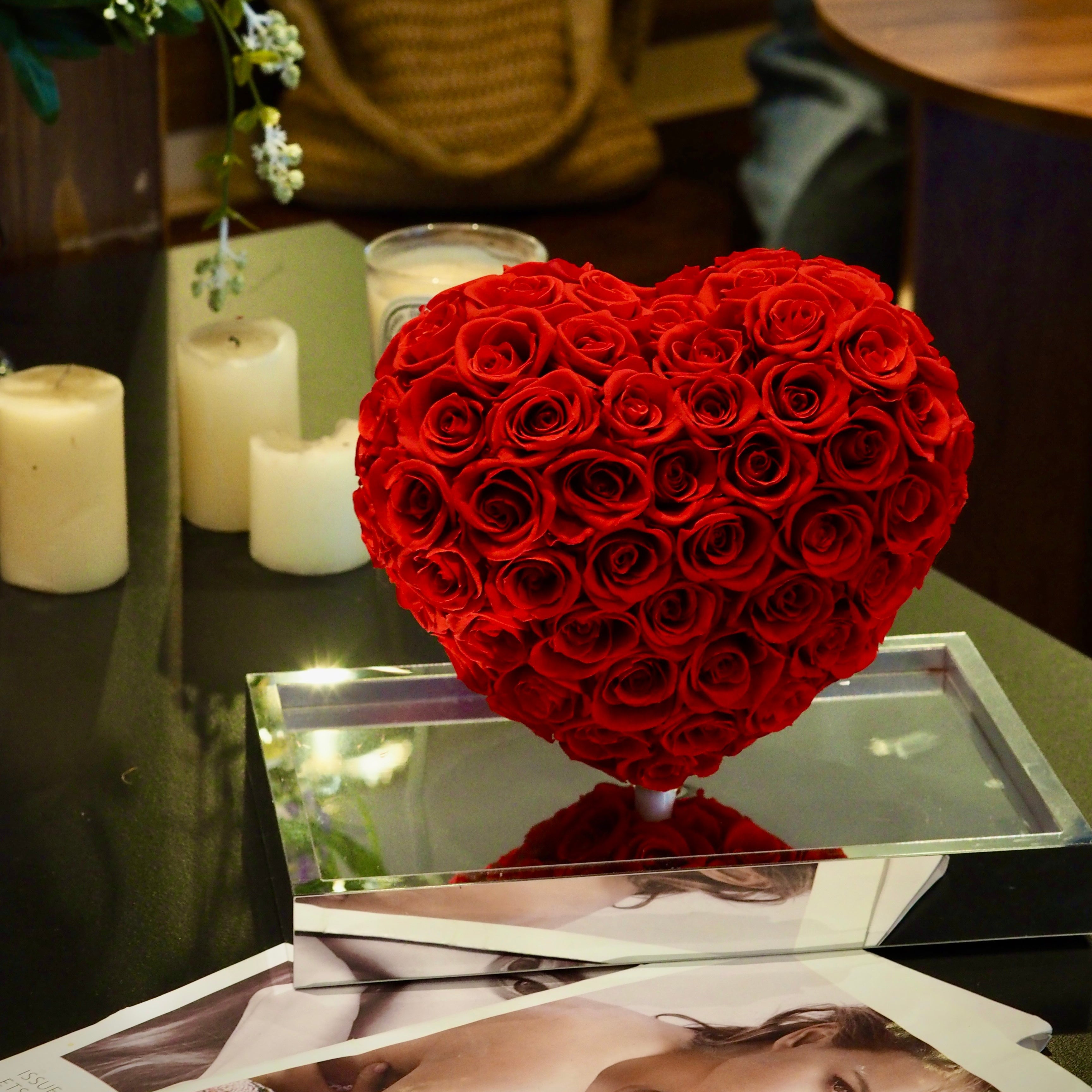 Heart-shaped arrangement of red roses on a table with candles and a photo album.