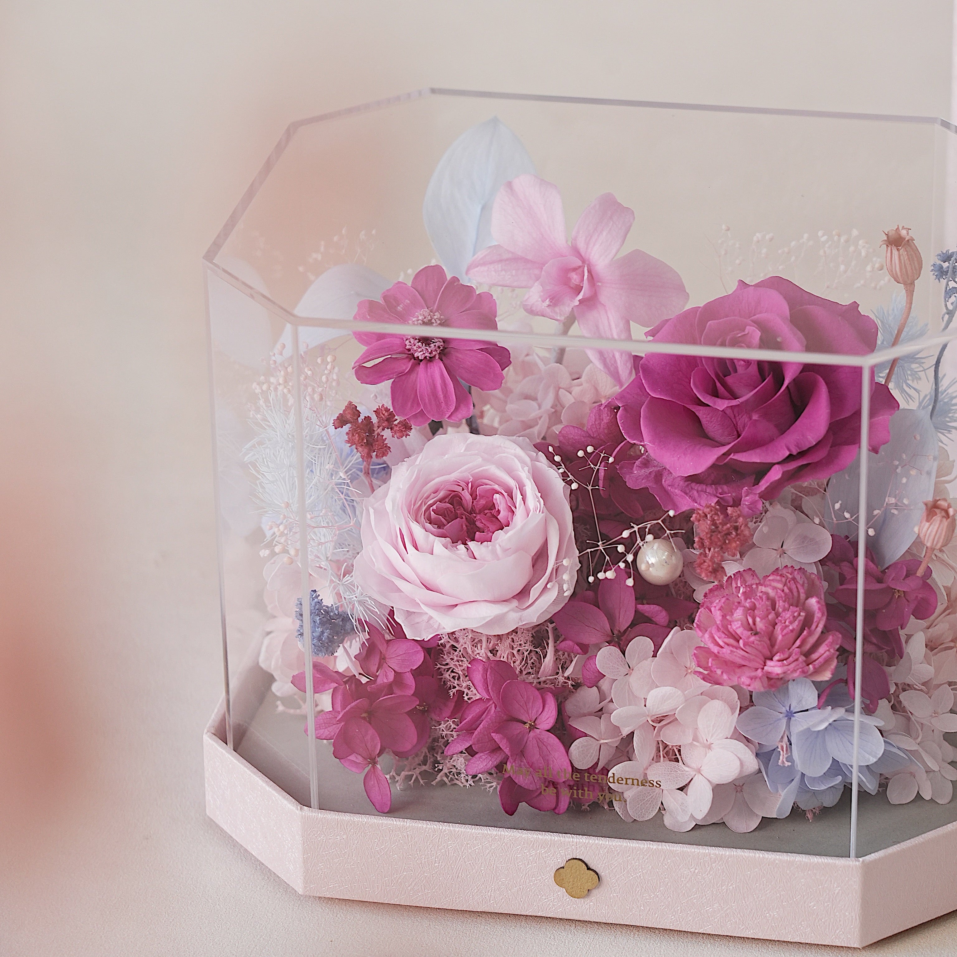 Hexagonal glass display box with pink and purple flowers on a light background