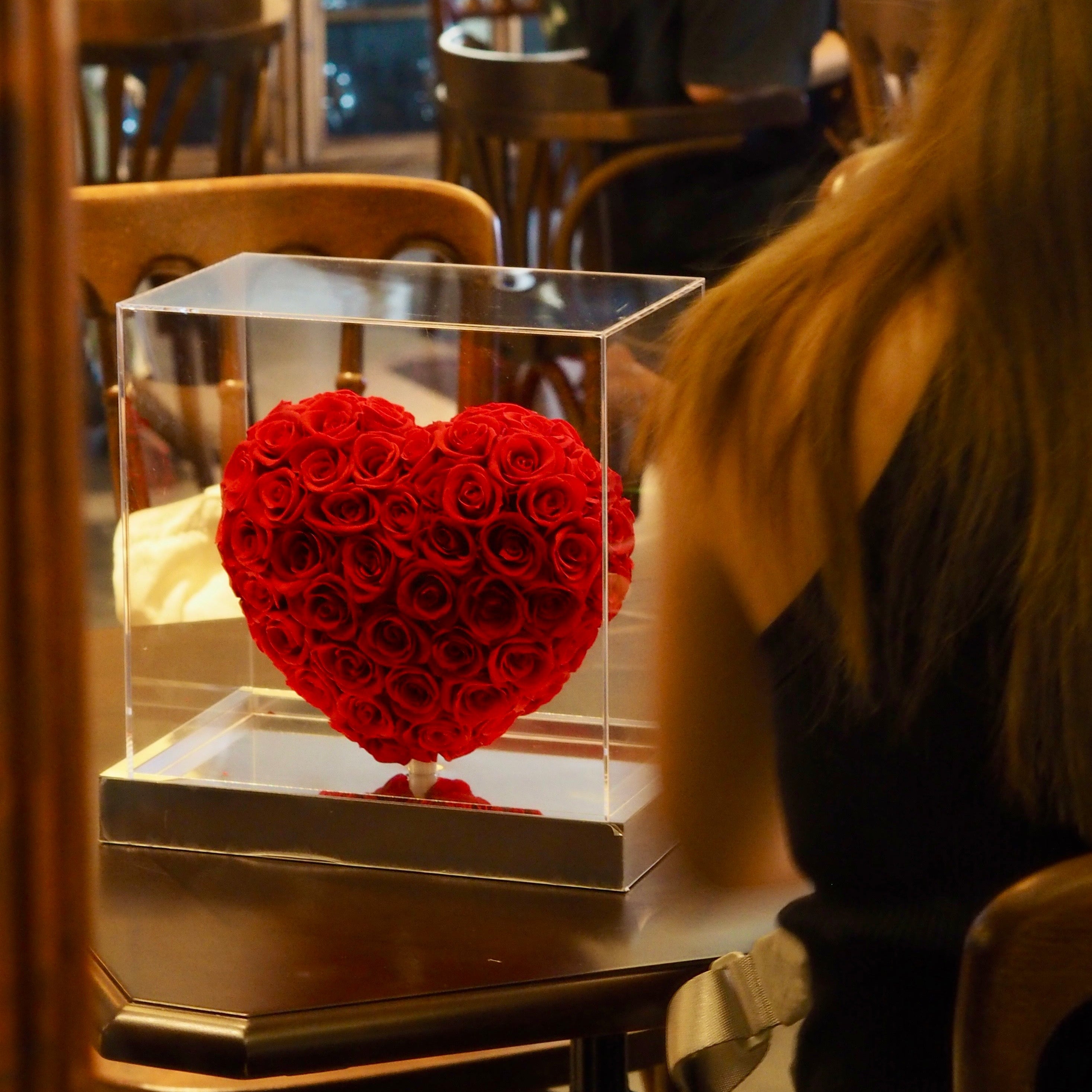Heart-shaped arrangement of red roses in a clear box on a table in a restaurant setting.