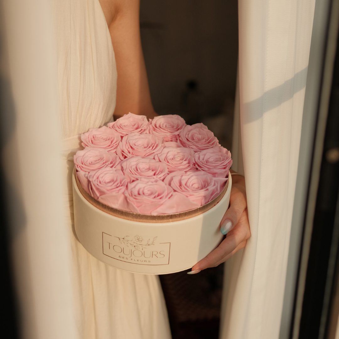 Person holding a round box of pink roses with 'L'oves' branding.