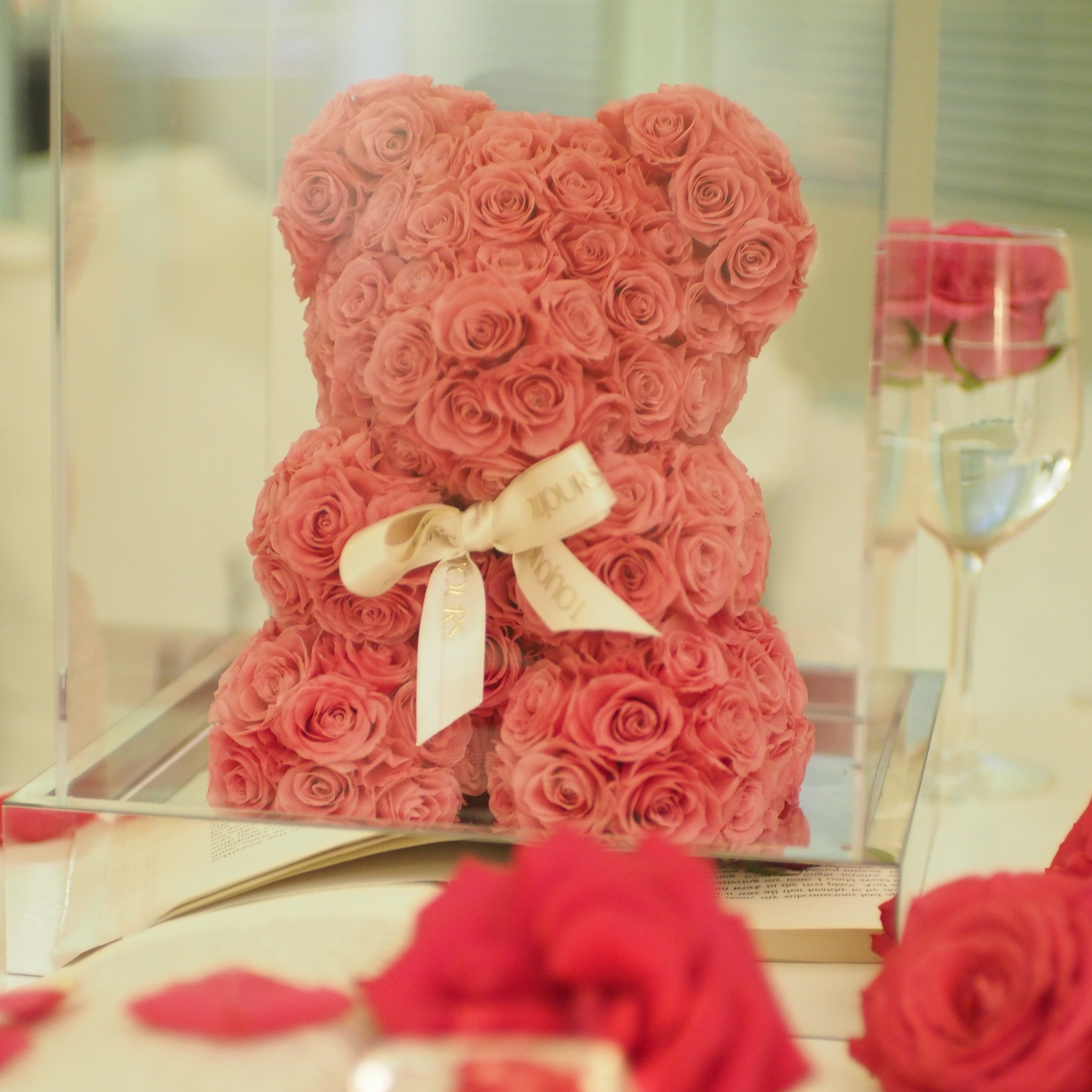 Heart-shaped arrangement of red roses with a bow on a reflective surface