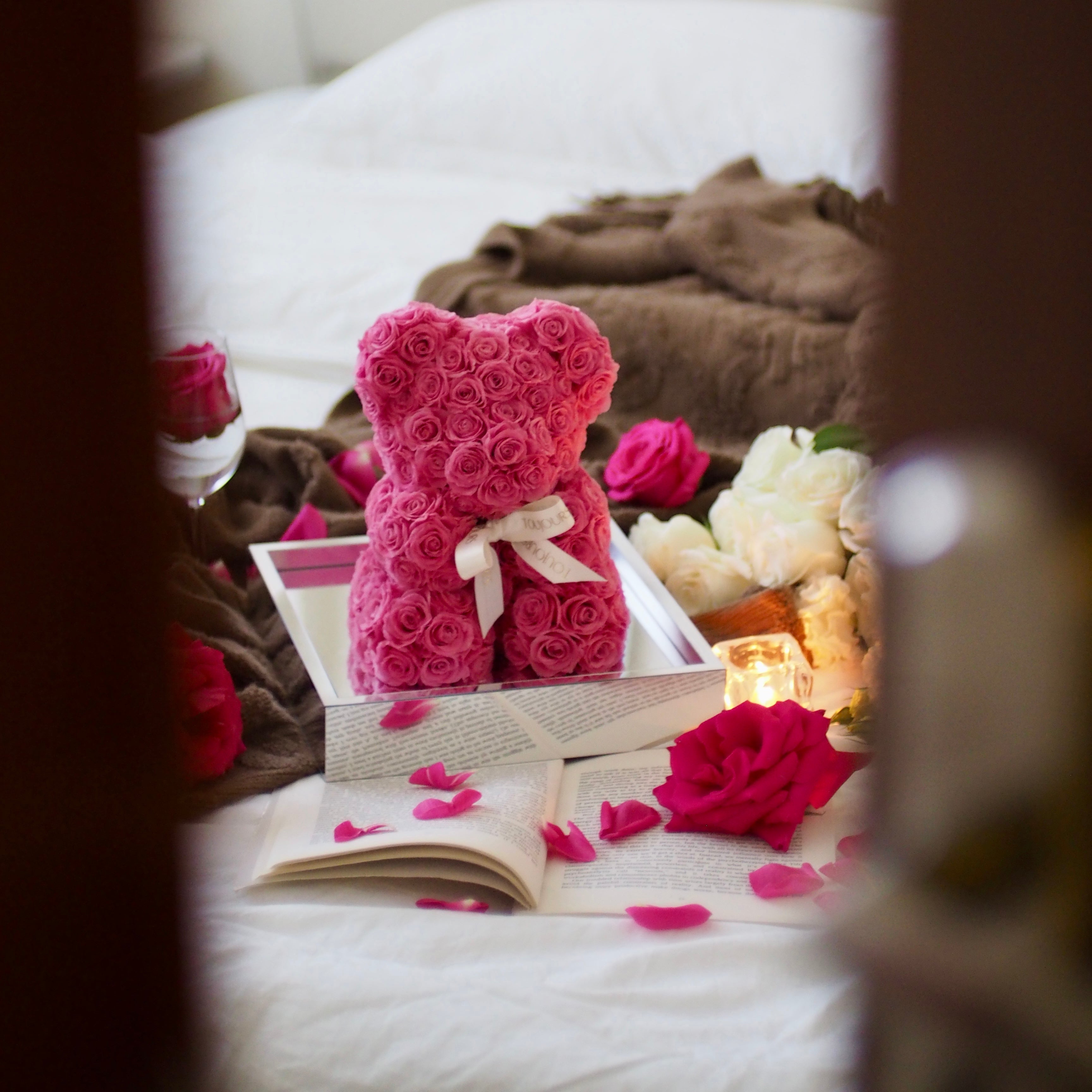 Pink teddy bear made of roses on a bed with candles and flowers