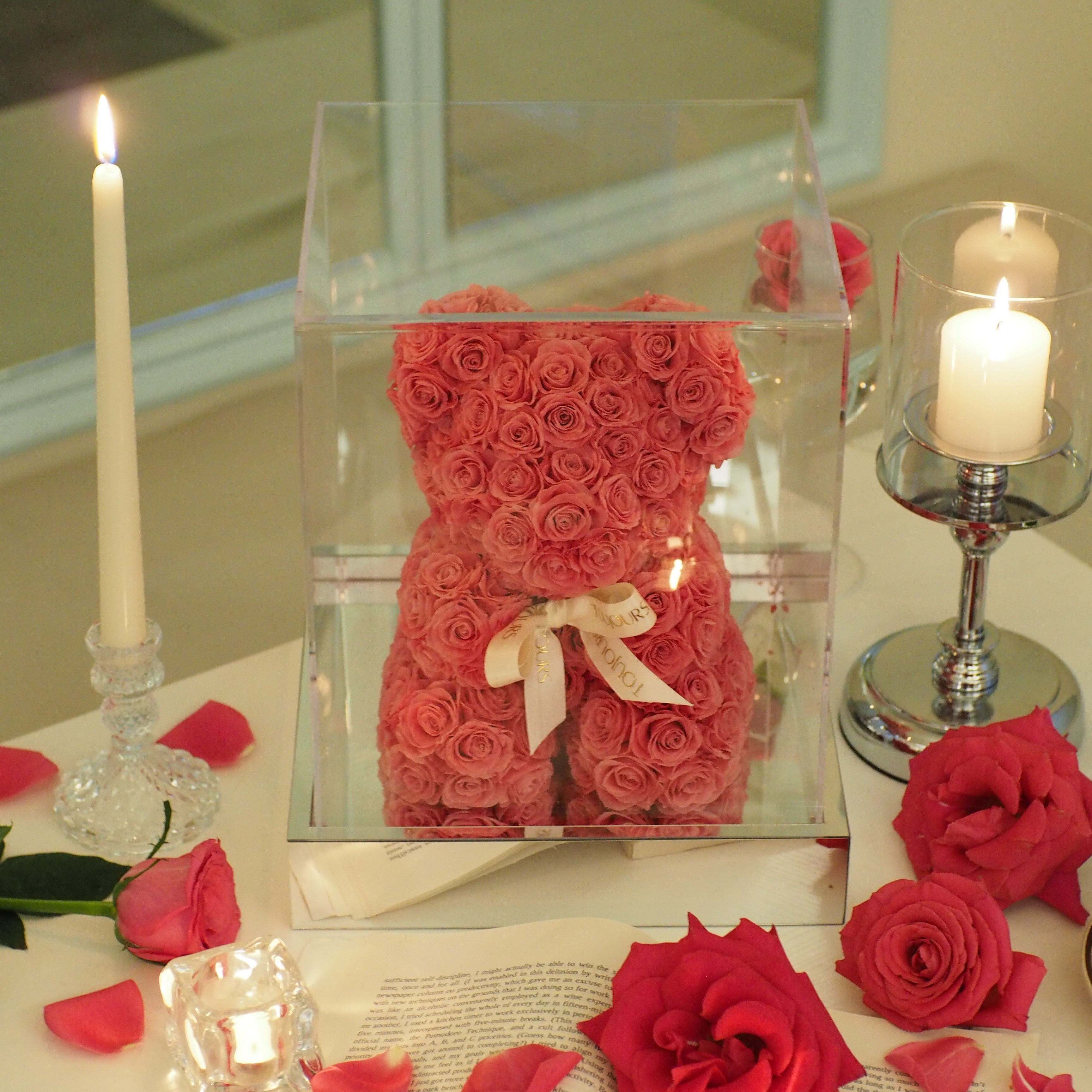 Decorative arrangement with red roses and a candle on a reflective surface.