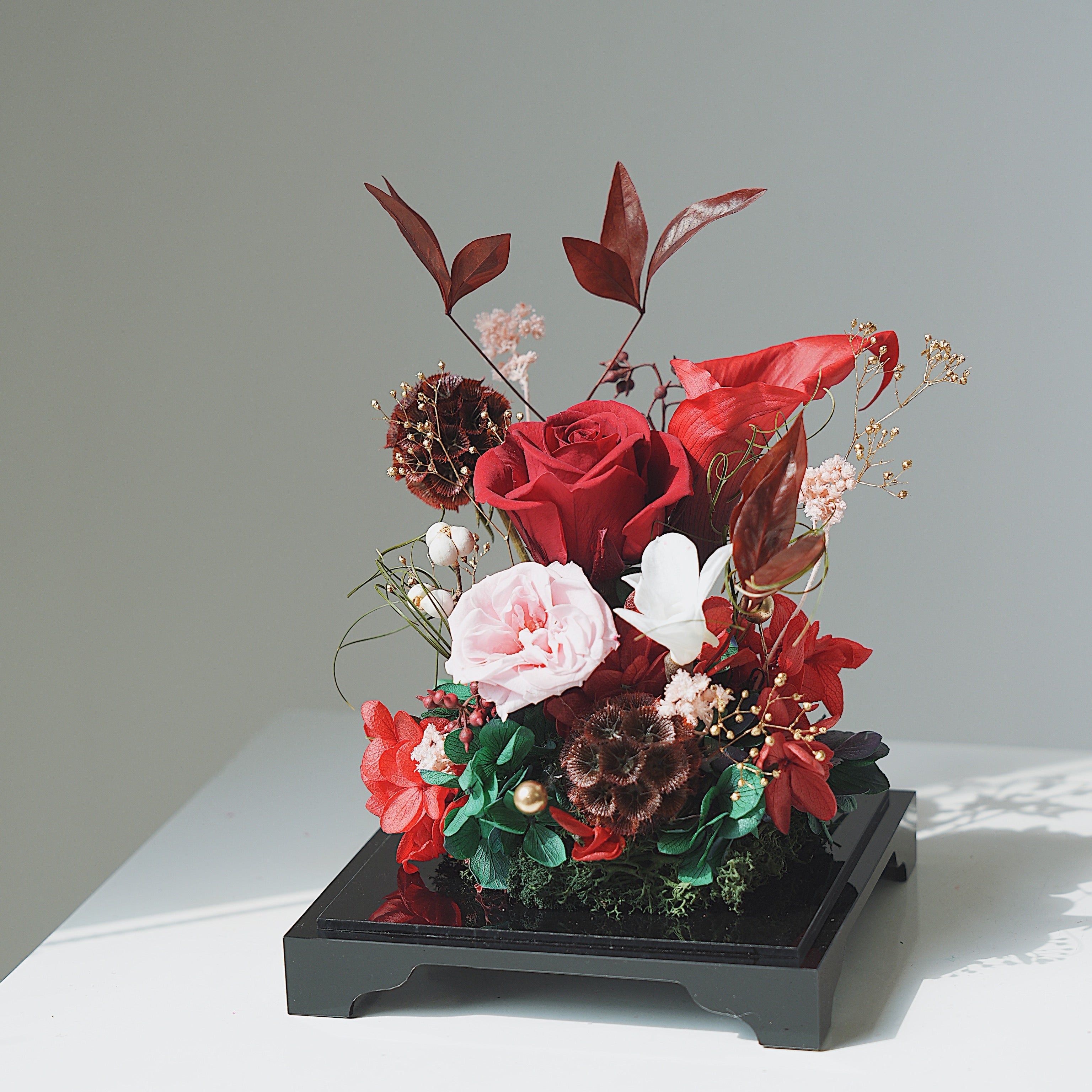 Floral arrangement with red and pink flowers on a black stand against a light gray background