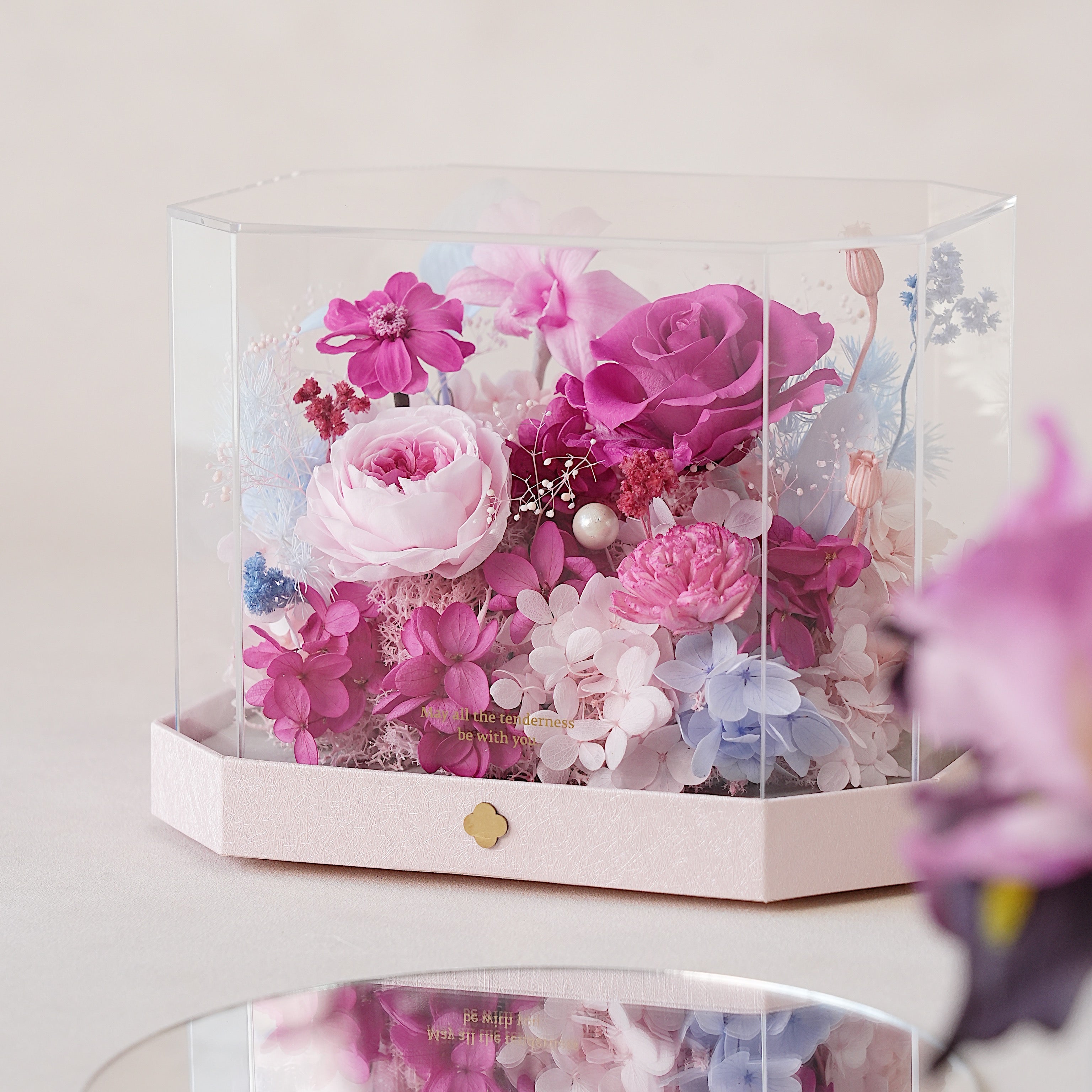 Transparent box with preserved pink and purple flowers on a light background