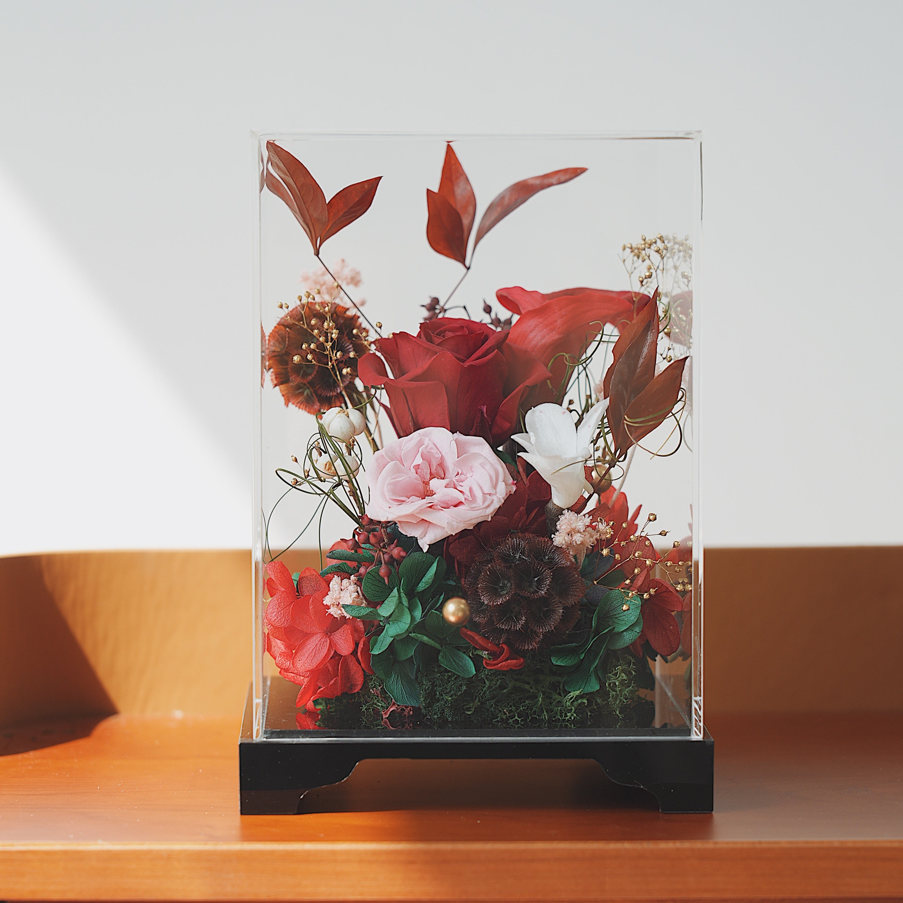 Glass display case with preserved flowers on a wooden surface