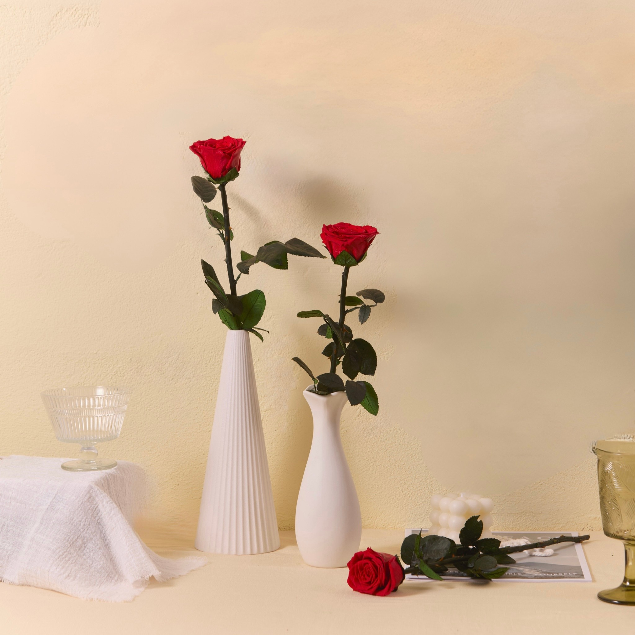 Two white vases with red roses on a beige surface.
