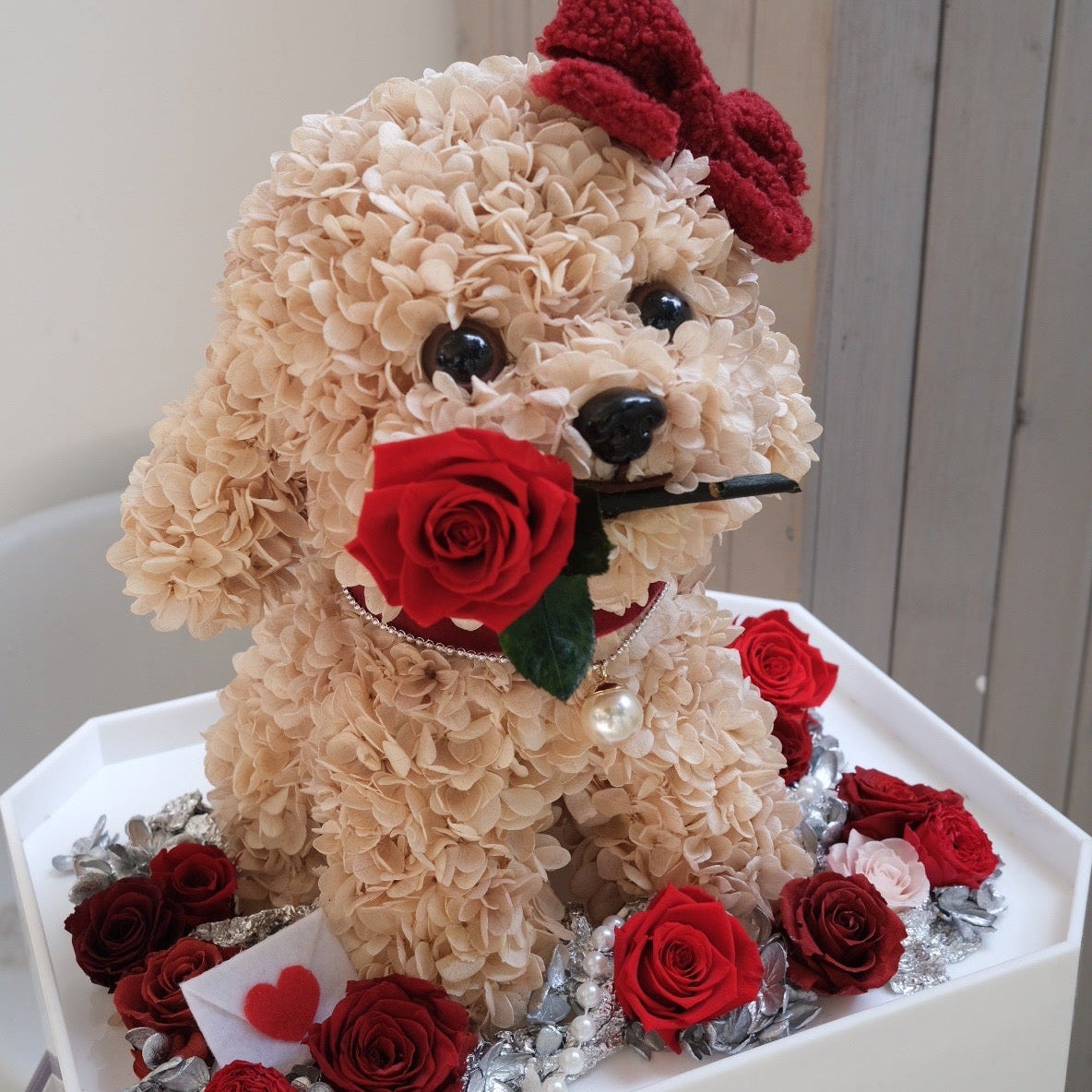 Decorative flower dog sculpture with red roses and a bow on a white base.