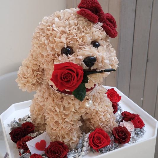Decorative flower dog sculpture with red roses and a bow on a white base.