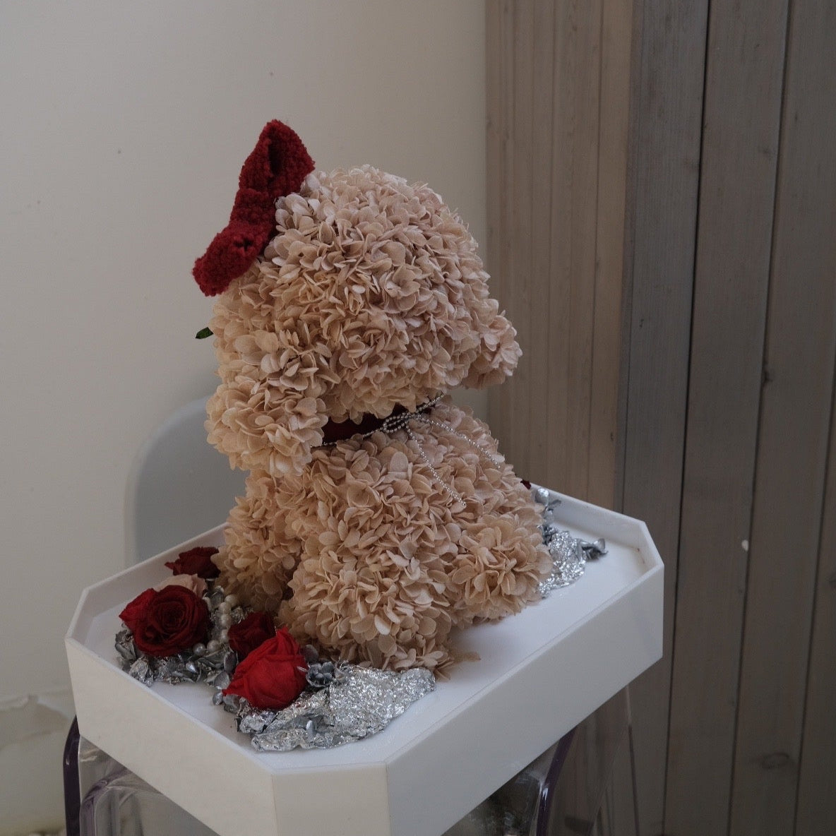 Floral Doggy Brown Poodle with red bow on a small white stand against a neutral background