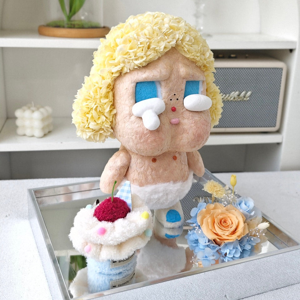 Flower Crybaby-baby blonde with blonde hair and blue eyes on a reflective surface with flowers and a plant in the background.