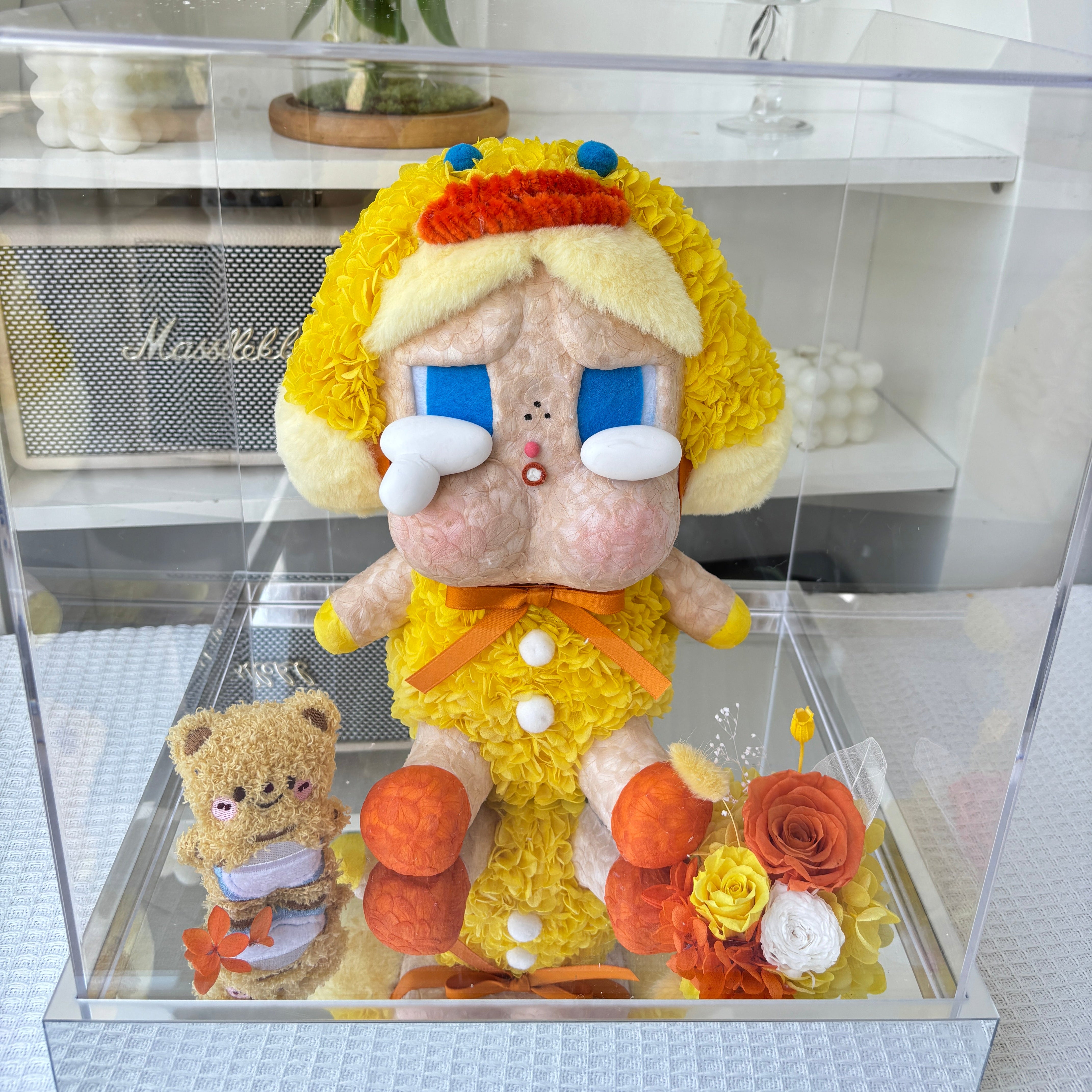 Flower Crybaby-duck you including a teddy bear, flowers, and a small boat inside a glass display case.