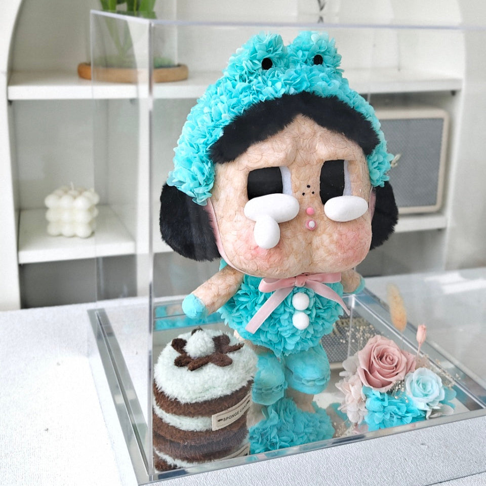 Flower Crybaby-what a frog with blue hair and outfit on a glass stand with flowers and a cake in a modern interior setting.