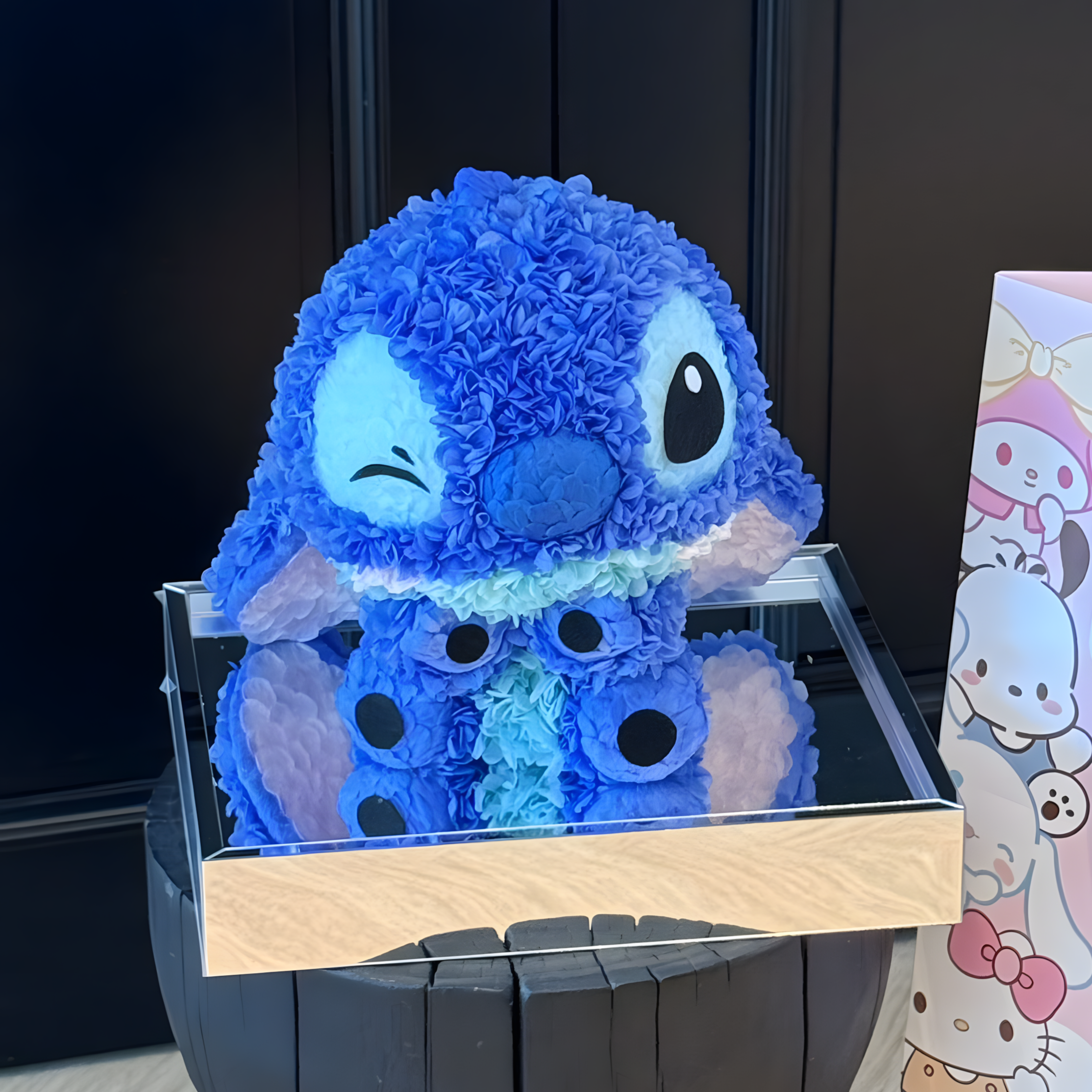 Blue plush toy resembling Stitch in a clear display case with a black background.