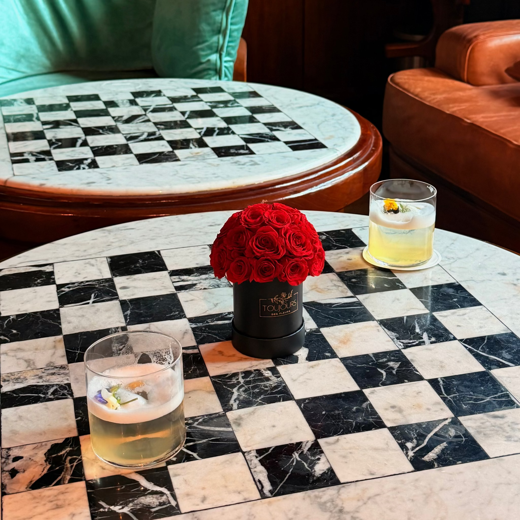 Checkered marble table with red roses and two drinks in a cozy room.