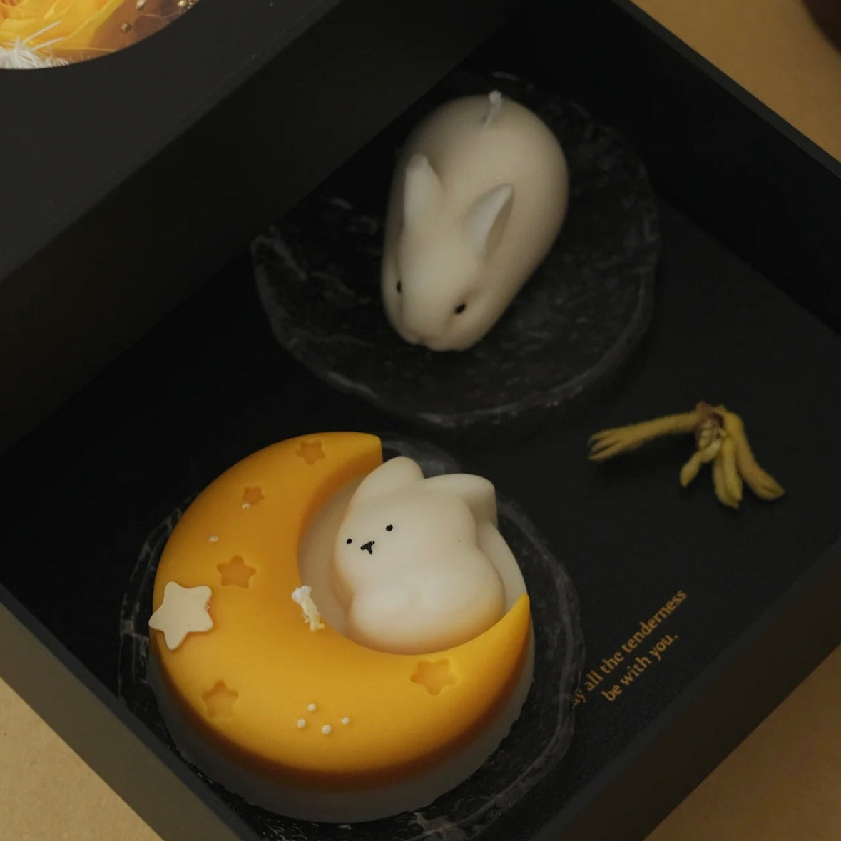 Decorative items including a white rabbit and ghost on a moon-shaped candles in a black box.