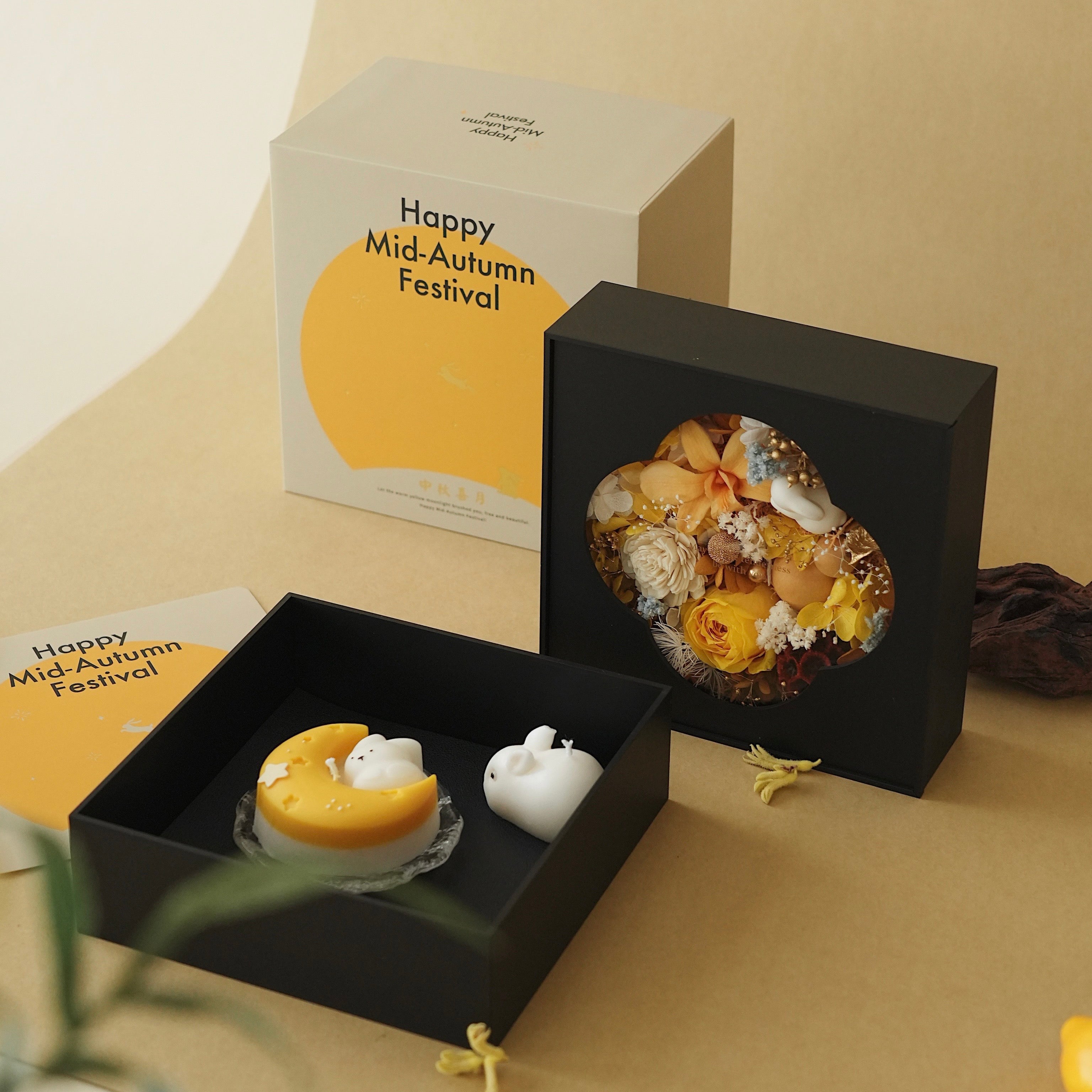 Decorative items for Mid-Autumn Festival in black boxes with 'Happy Mid-Autumn Festival' cards on a beige background.