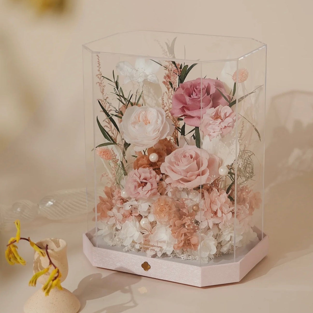 Hexagonal glass display case with preserved pink and white flowers on a soft beige background