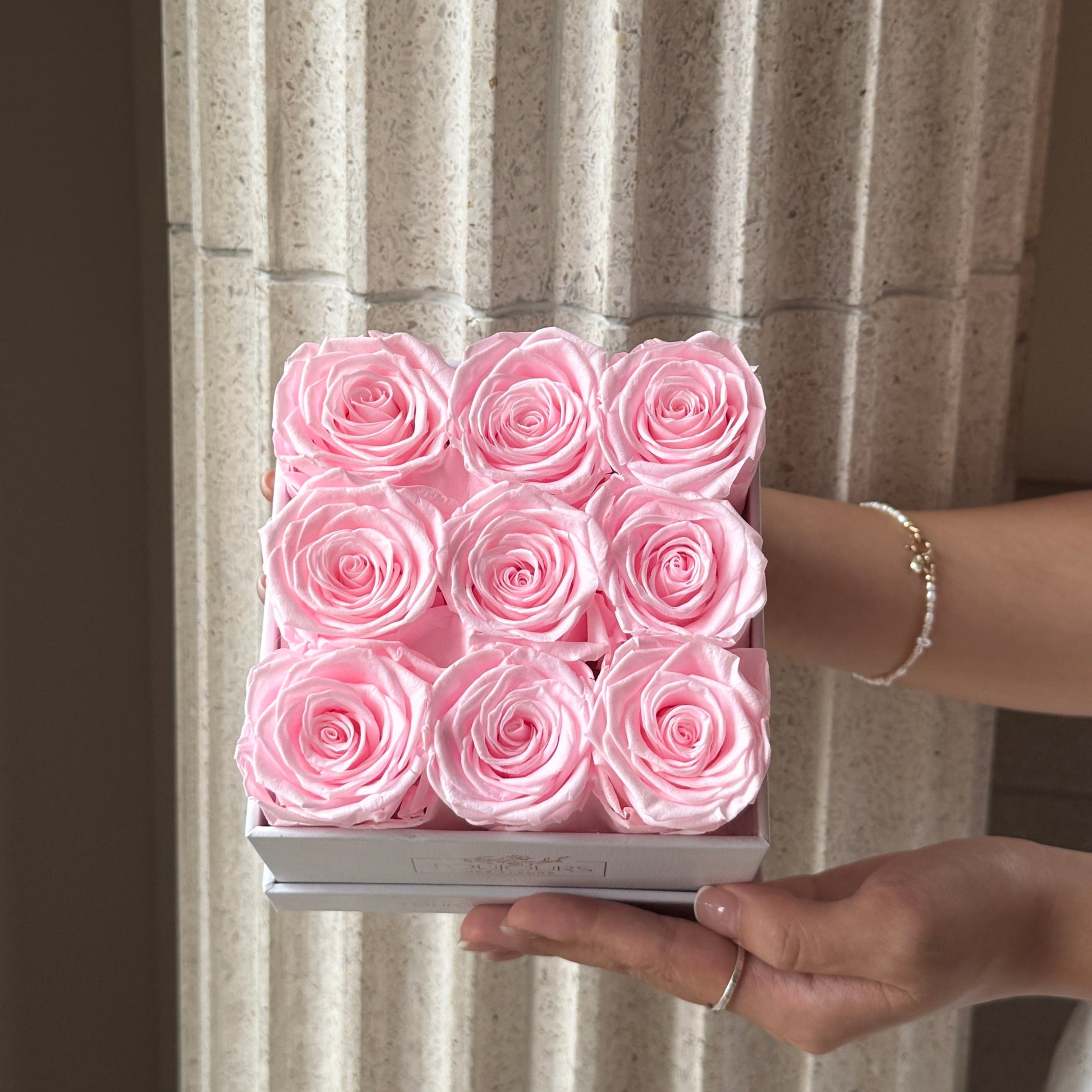 Person holding a box of pink roses against a neutral background