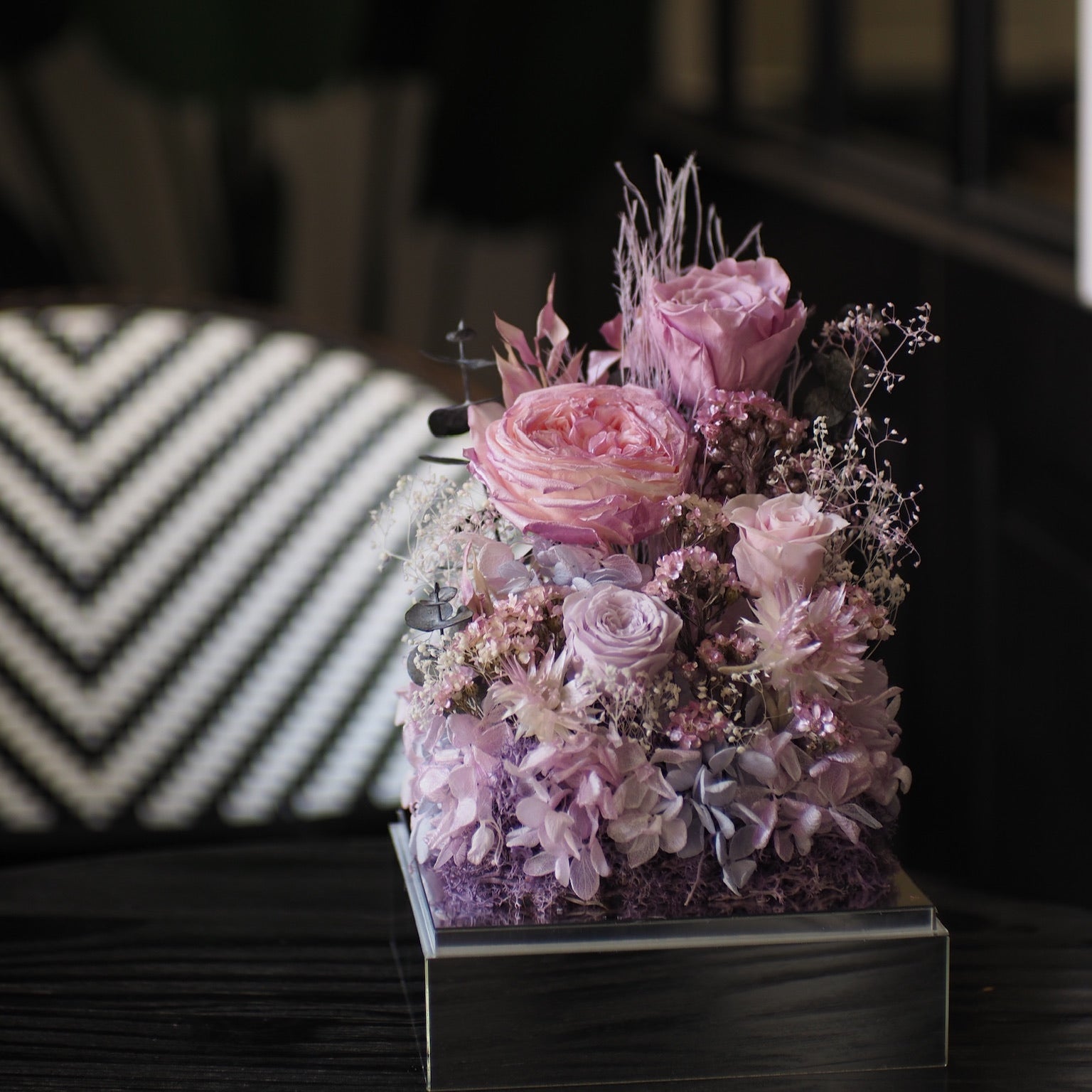 Decorative floral arrangement in a clear container on a dark surface with a blurred background