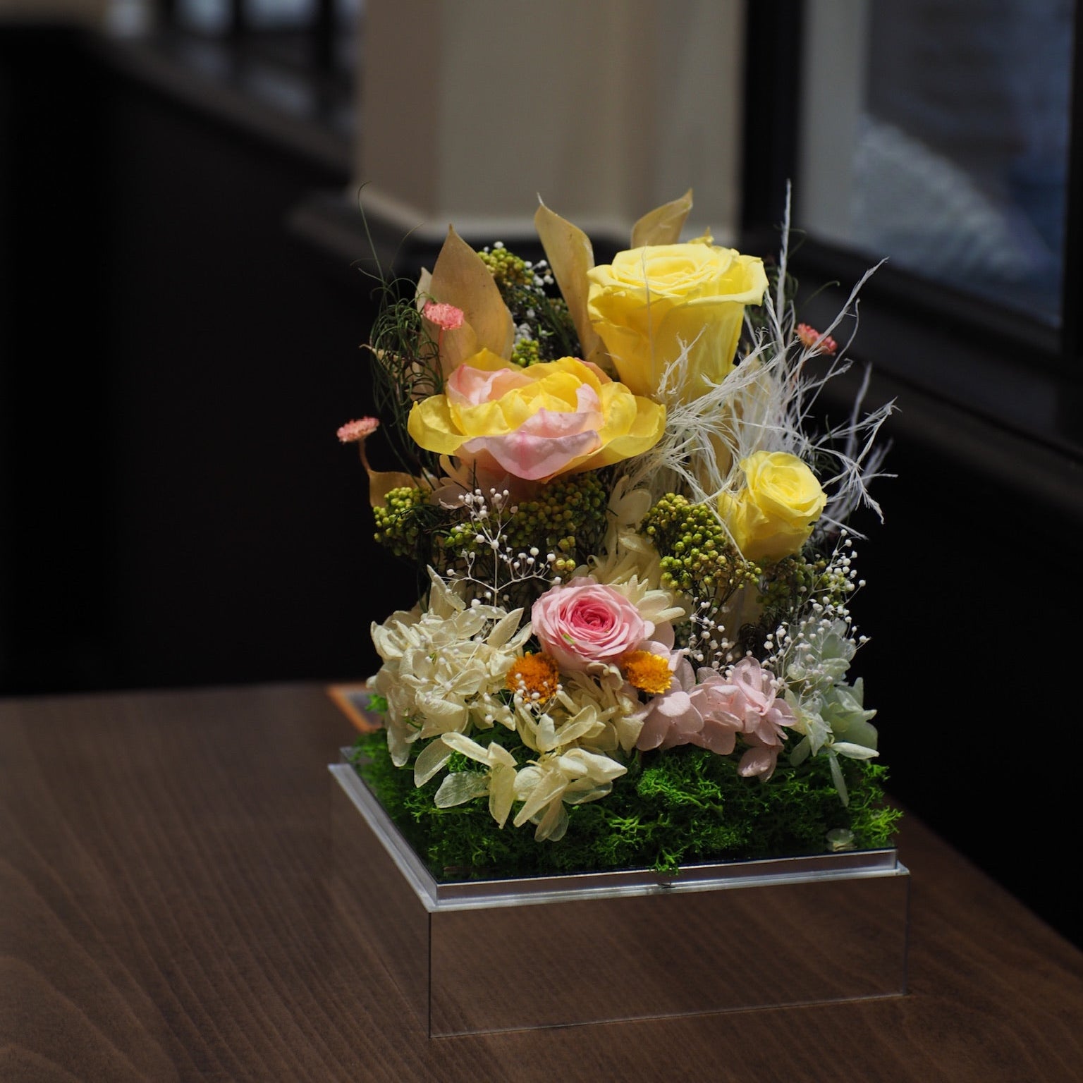 Floral arrangement with yellow and pink flowers on a wooden surface