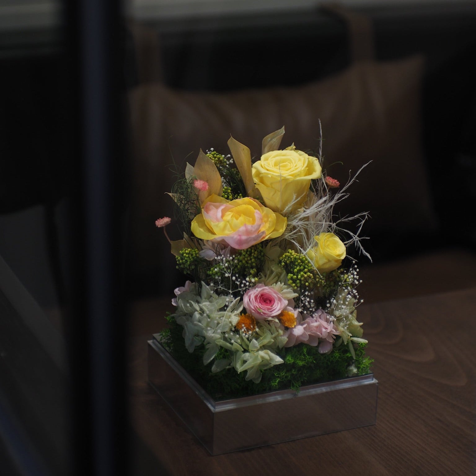 Floral arrangement with yellow and pink flowers in a pot on a wooden surface.