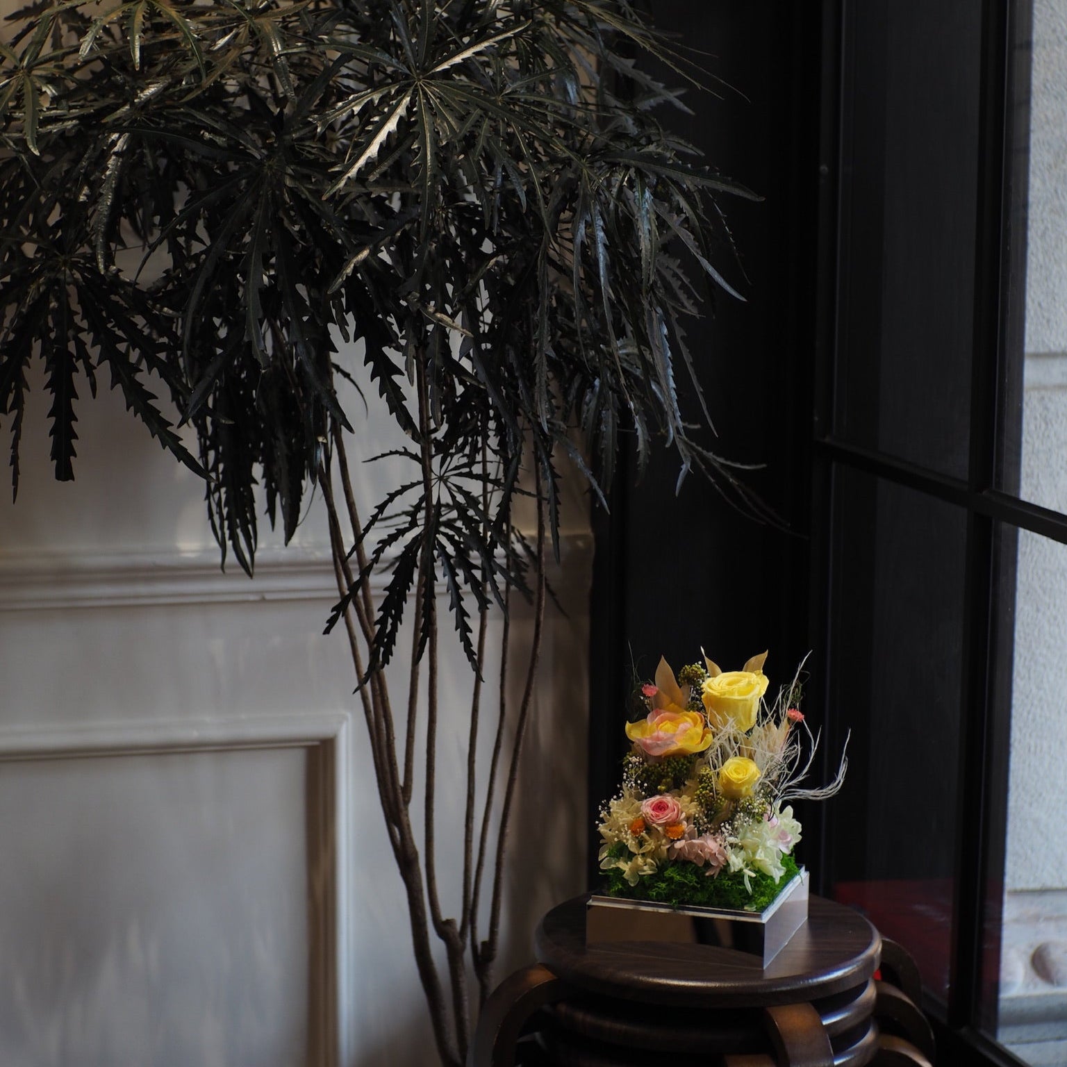 Decorative flower arrangement on a small table next to a tall potted plant indoors.