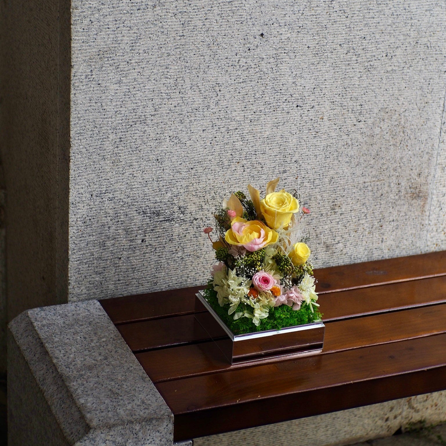Floral arrangement on a wooden bench against a textured wall.