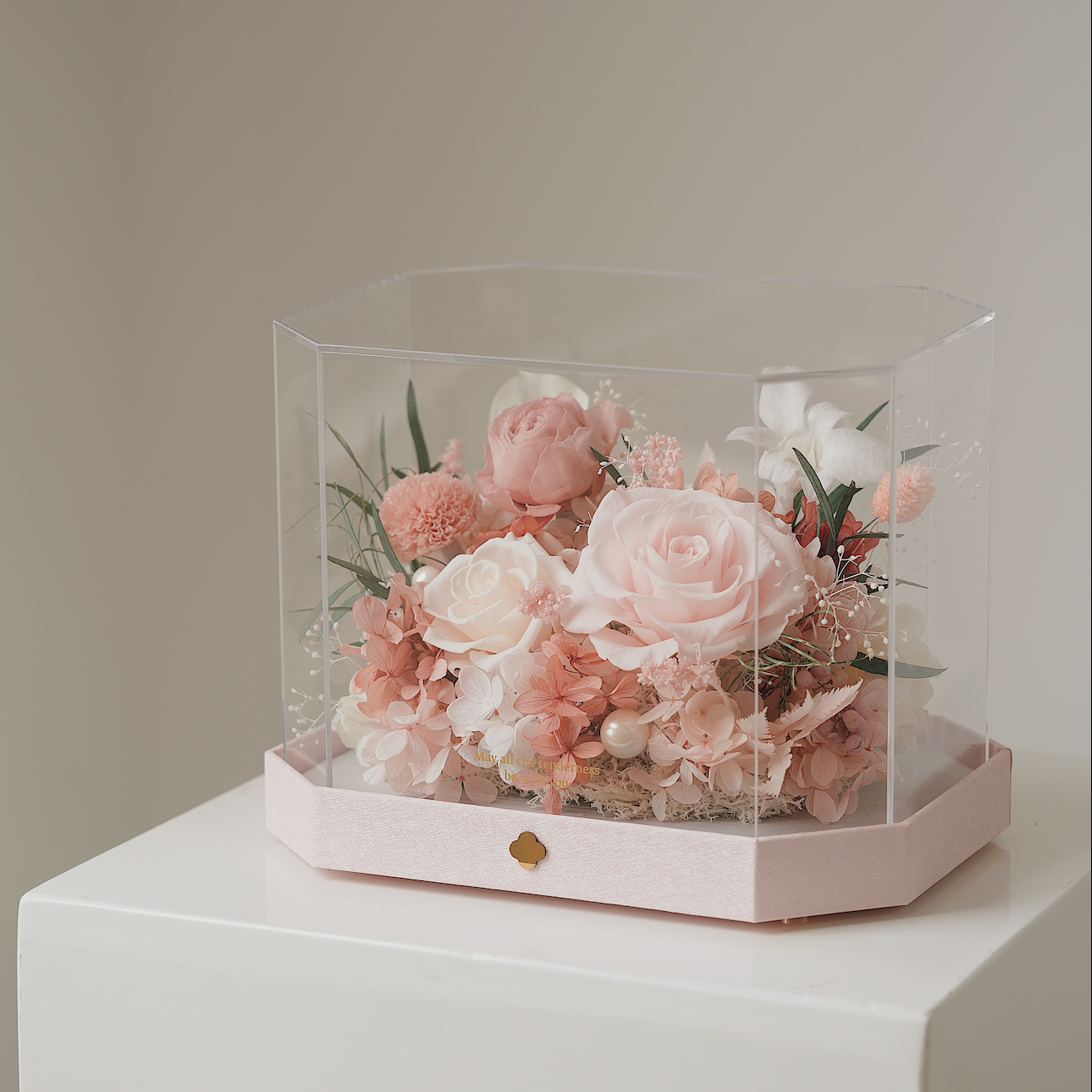 Hexagonal glass display case with pink and white flowers on a white surface.
