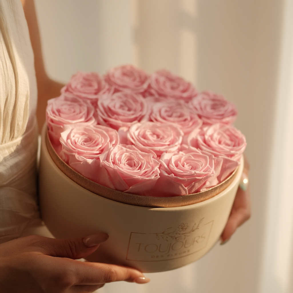 Round beige box filled with pink roses held by a person against a neutral background