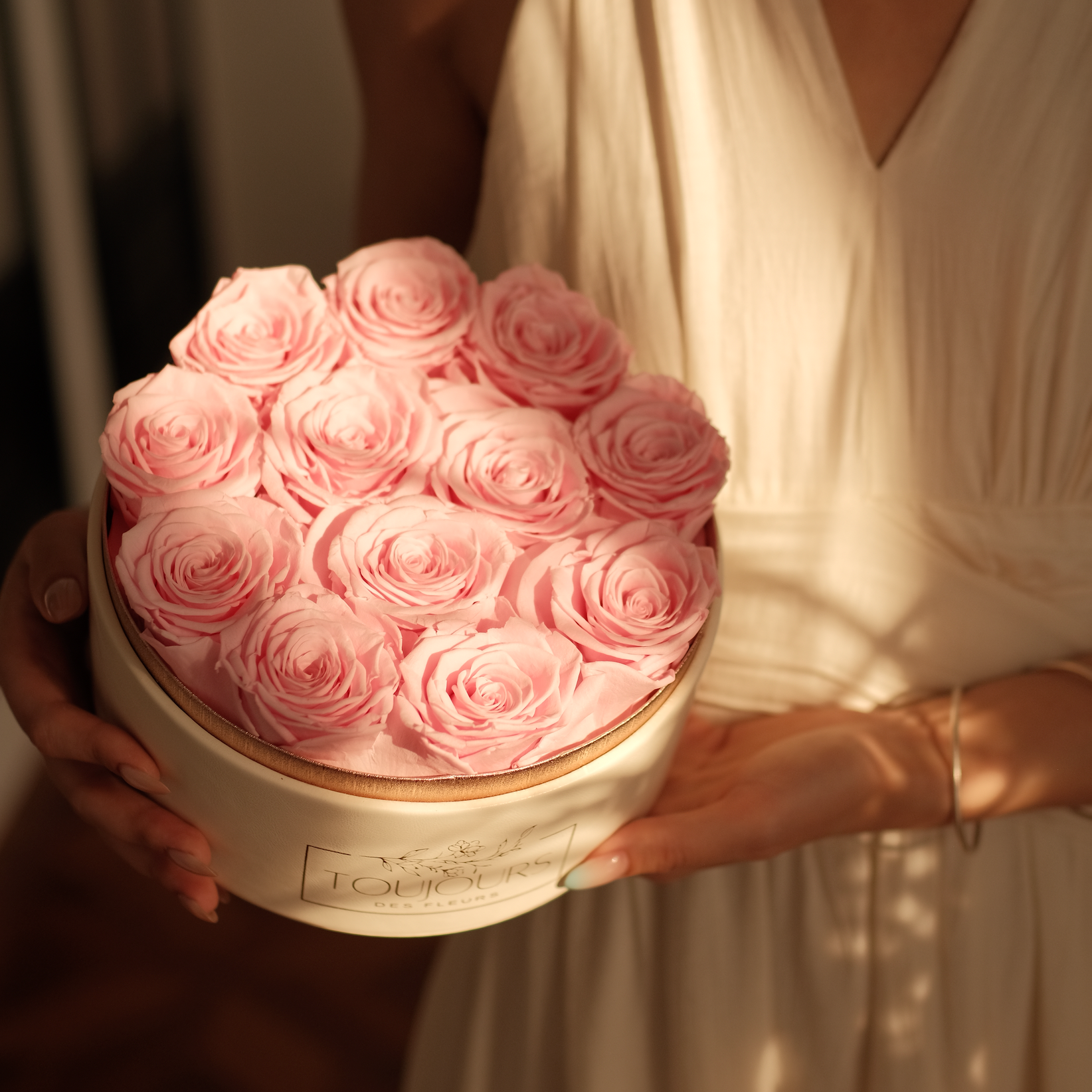 Person holding a box of pink roses with a blurred background