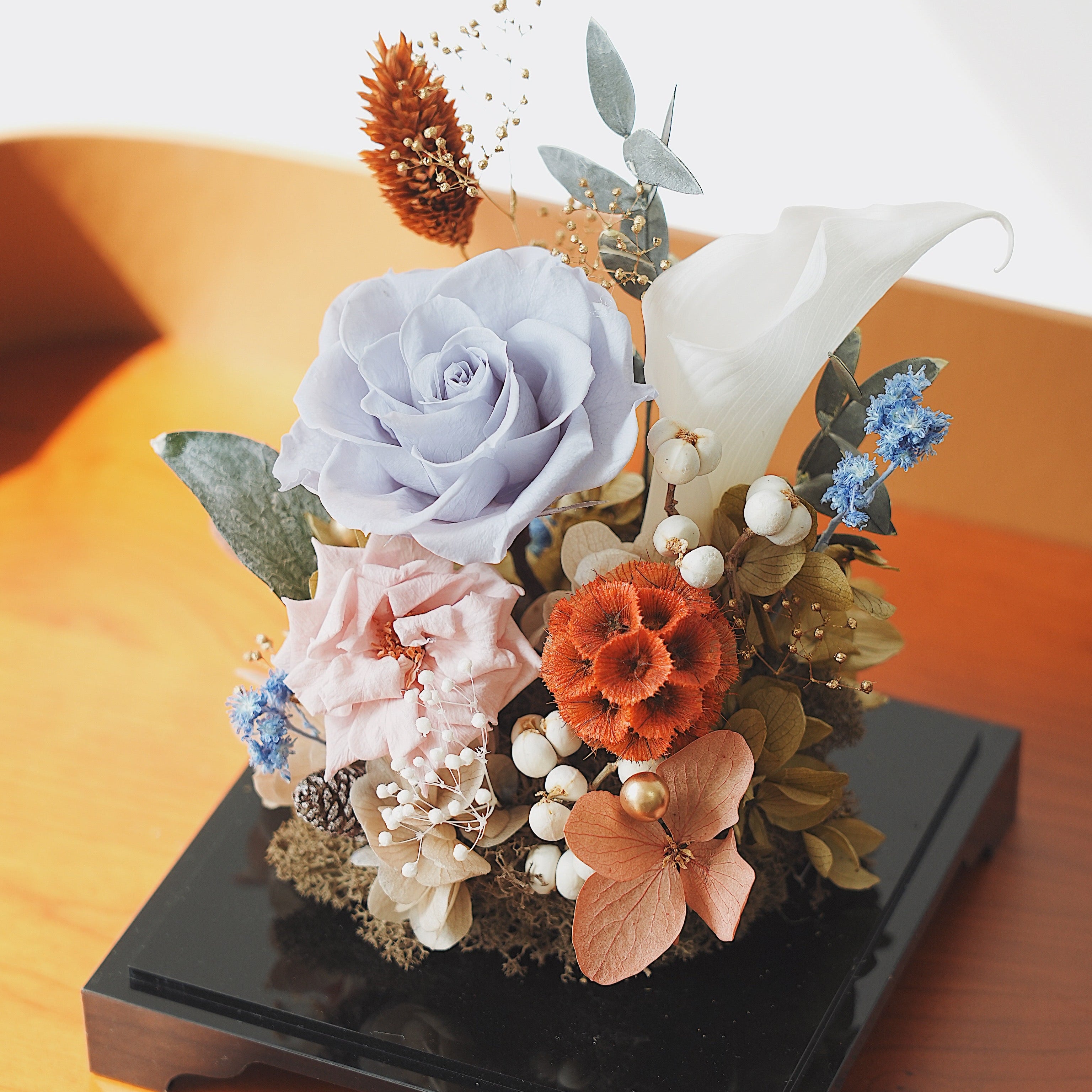 Decorative floral arrangement on a black base with a wooden surface background