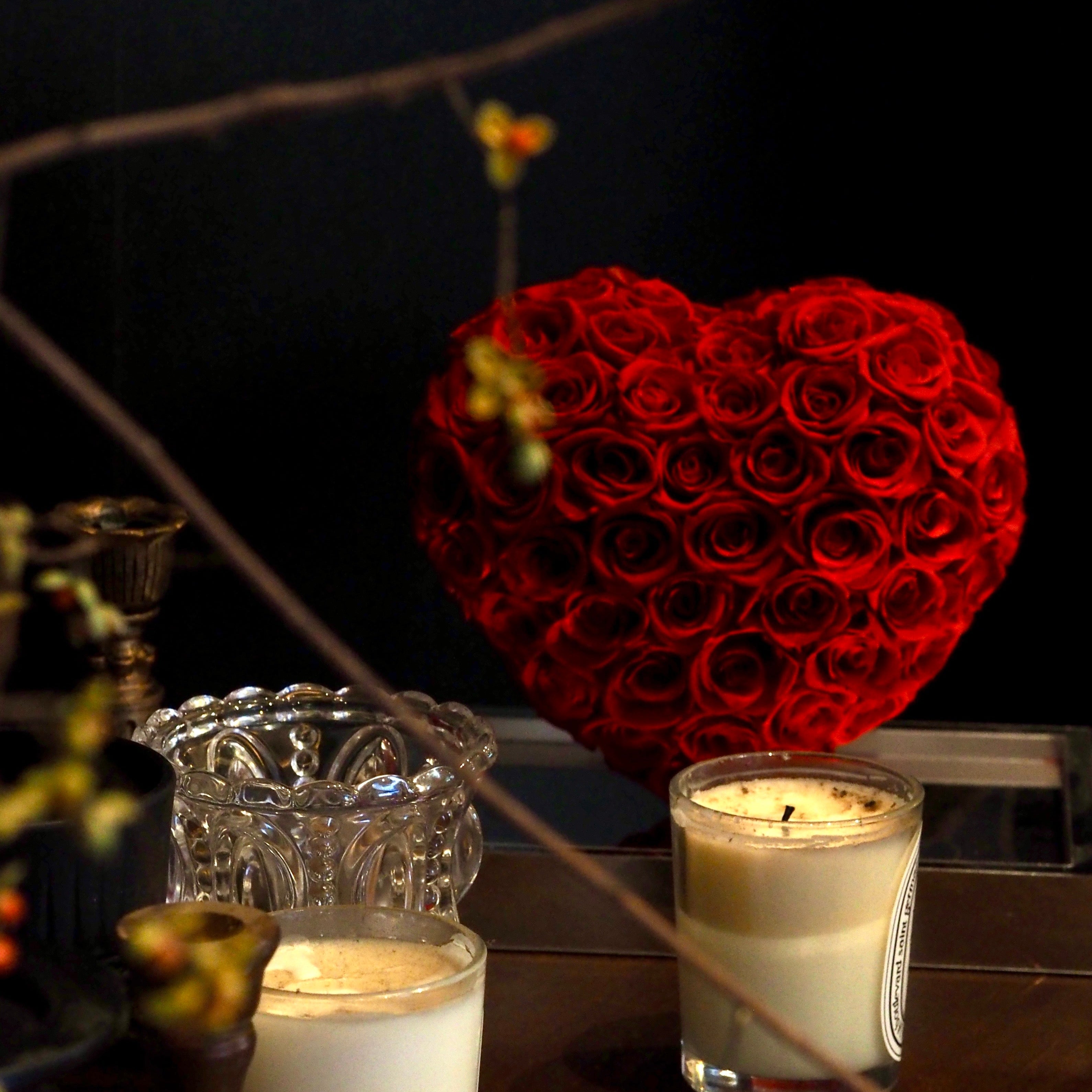Heart-shaped arrangement of red roses with two candles on a dark background