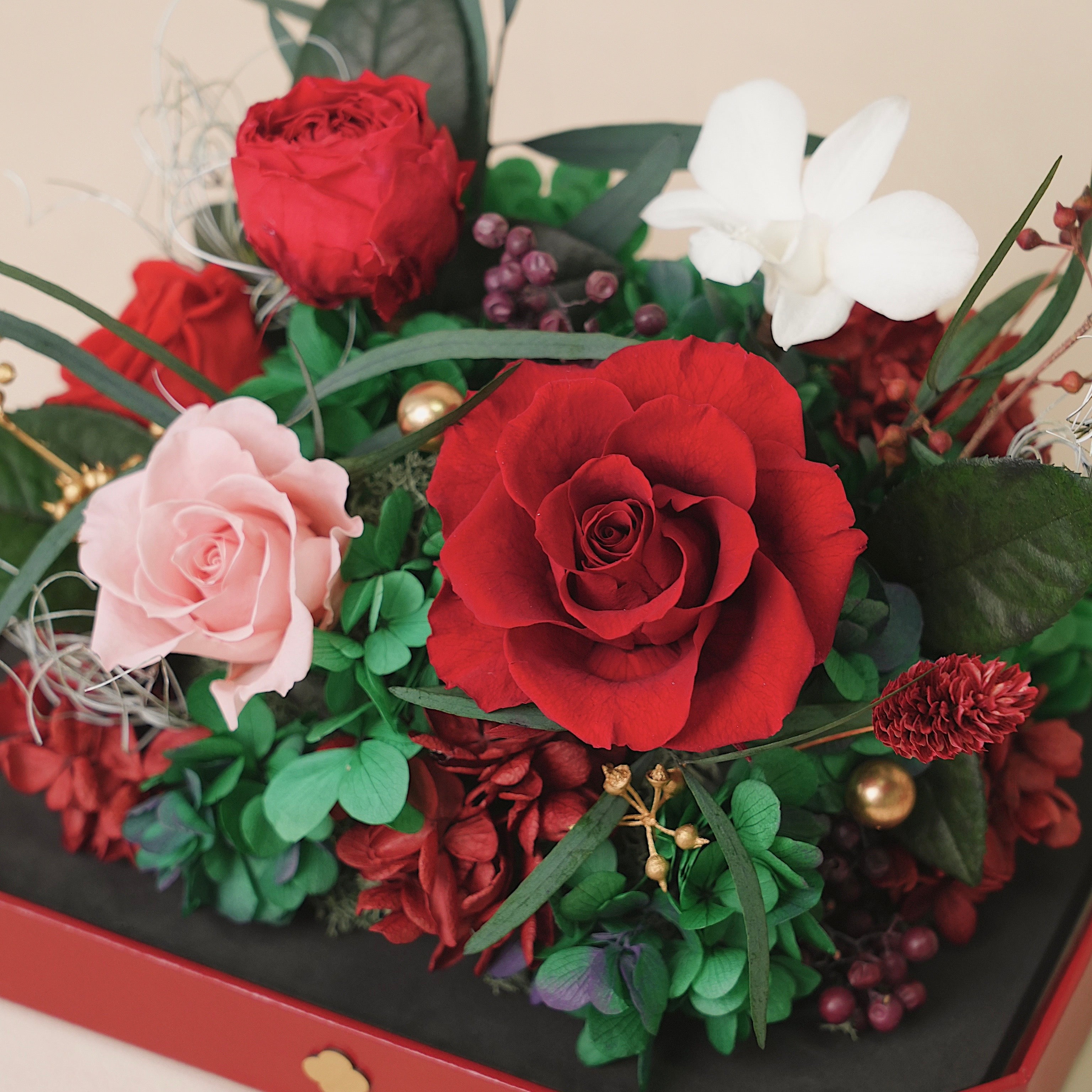 Bouquet of red and pink roses with greenery on a black box.